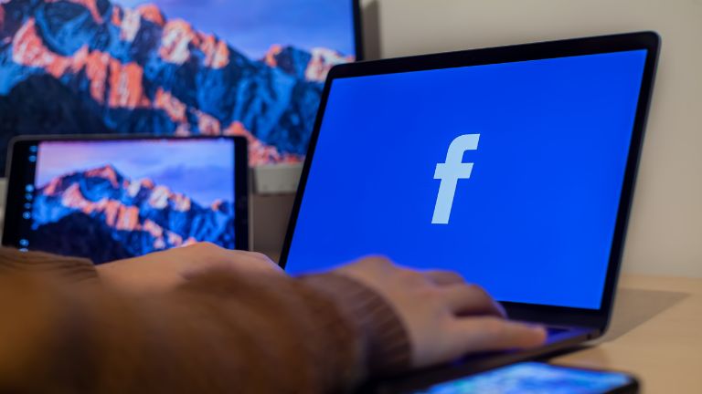 ekran komputera z niebieskim logo facebooka i ręka człowieka